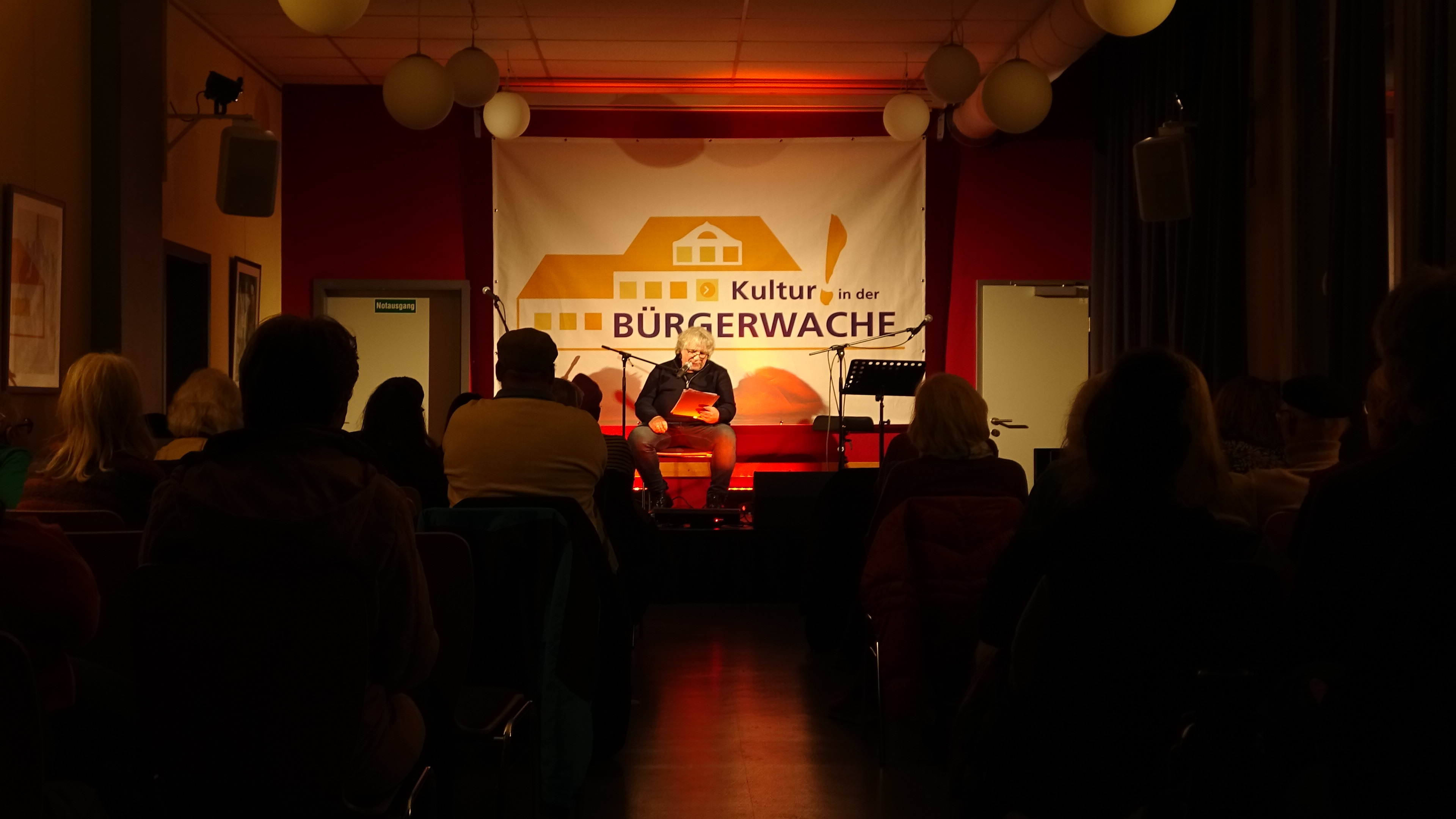 Kultur in der Wache - das Foto zeigt eine Lyrik Lesung mit Musik und dem Autor Hellmuth Opitz vom Dezember 2025